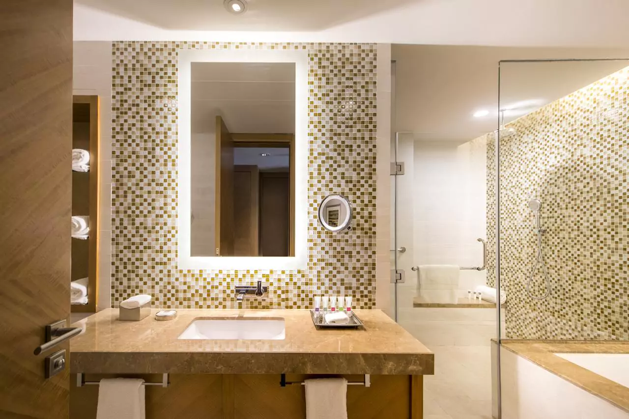 Fancy mosaic tiled bathroom with a shower room and lighted frosted mirror above a sink in Dubai.