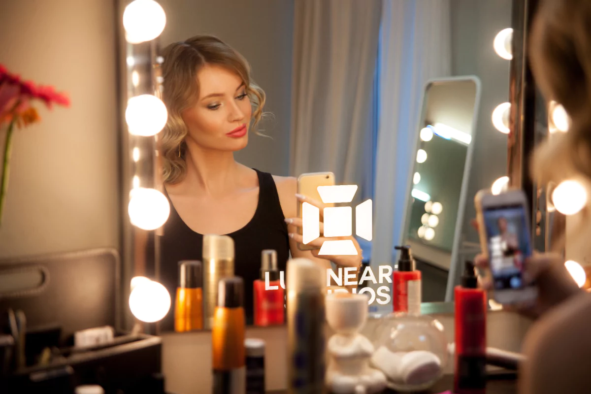 In front of a blazing logo on a Hollywood makeup mirror, a woman is taking a selfie from Dubai.