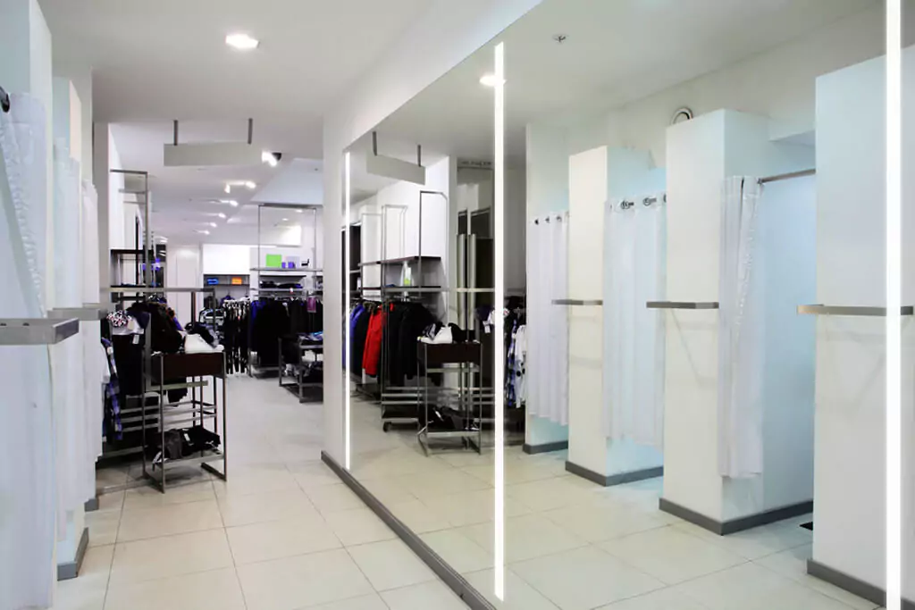 Fitting room area in a clothing store in Dubai with a big vanity mirror mounted on a concrete wall.