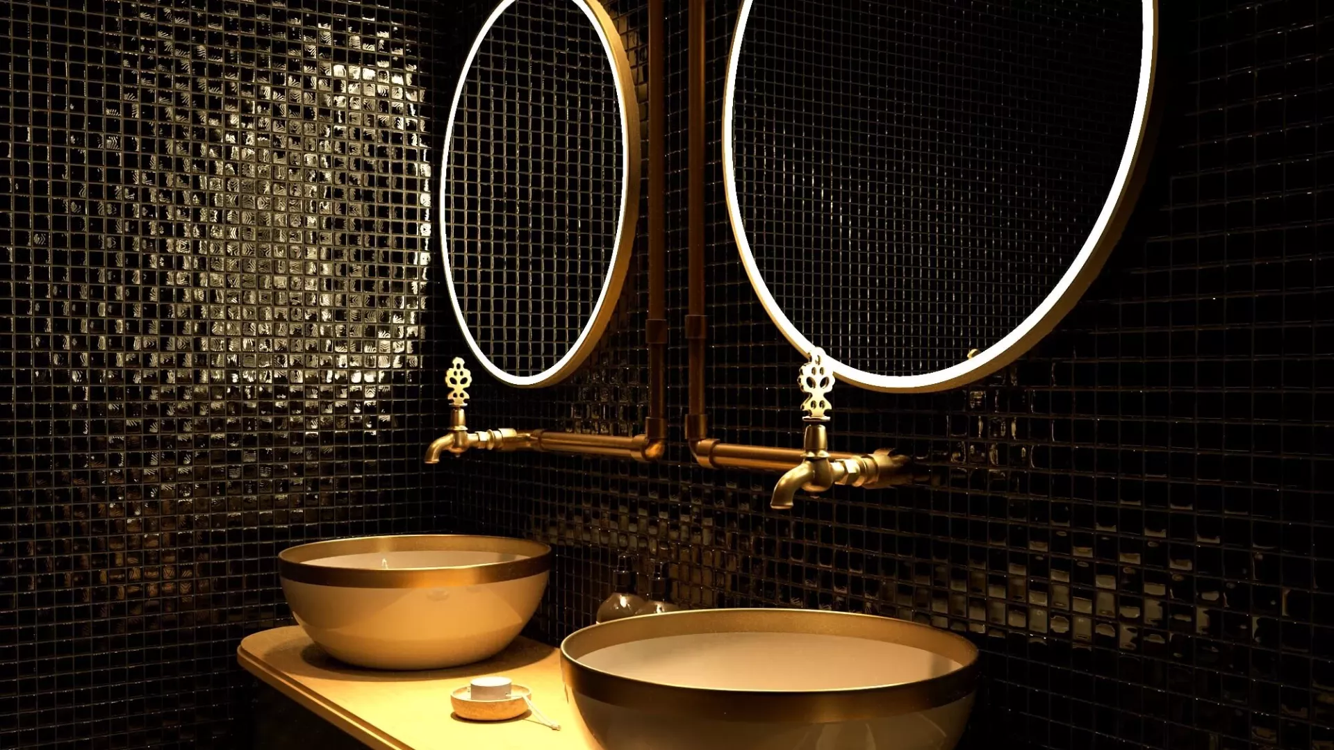 Pair of gold oval lit mirrors on a black mosaic tiled wall with to gold sinks and faucets in Dubai.