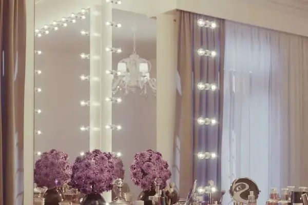 Vanity mirror with light bulbs above a table with makeup materials in a dim lighted room in Dubai.