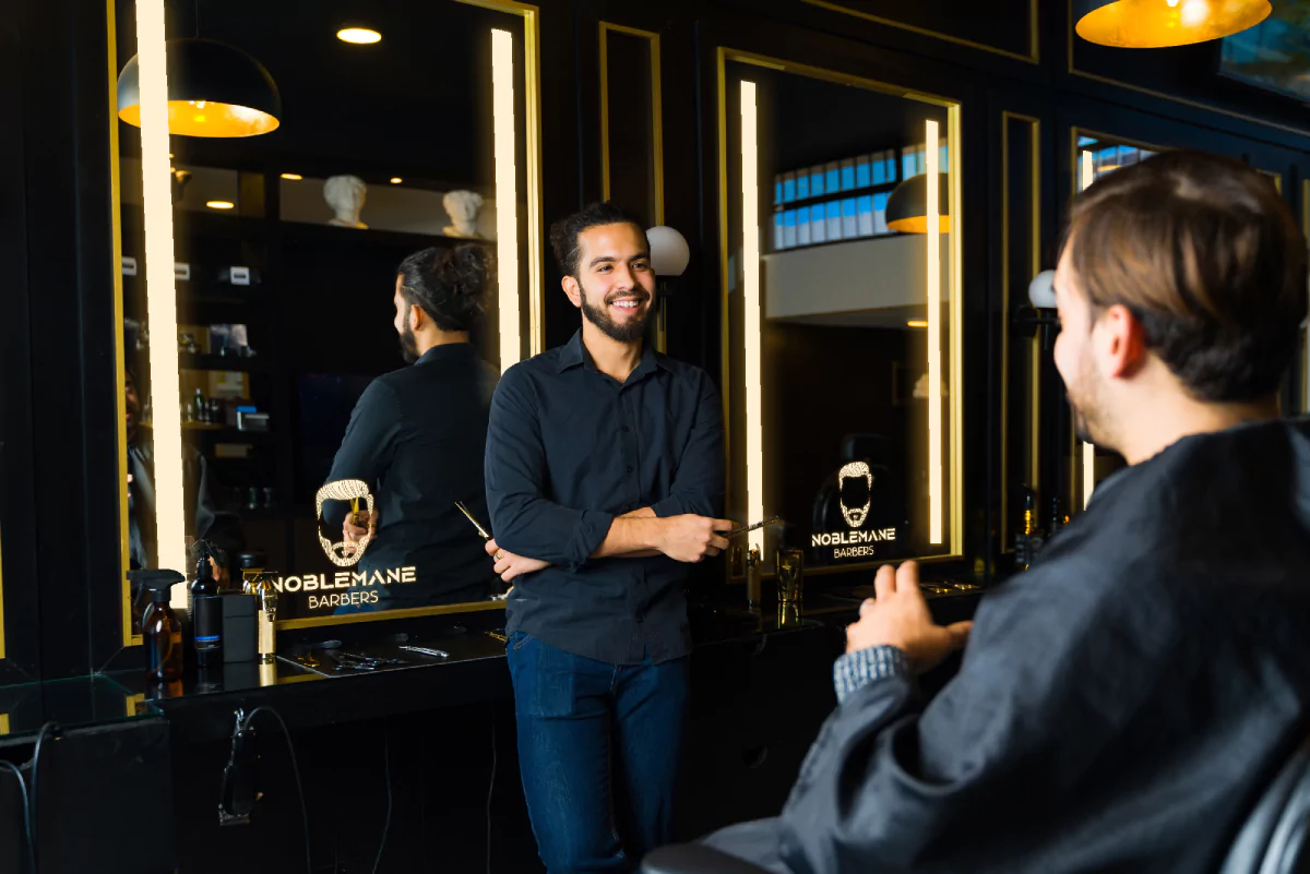A classy barbershop with a bright logo in a lit make up mirror, two men deep in talking from Kuwait.