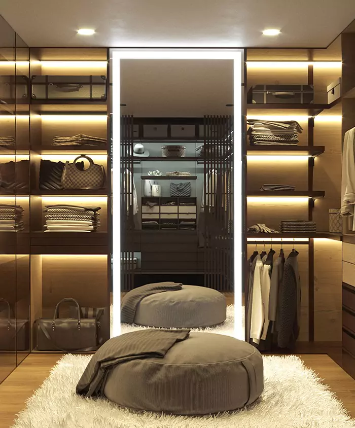 Walk in closet in Kuwait with shelves full of folded clothes and a lighted mirror in the middle.