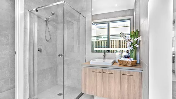 Tiny of bathroom with a shower room beside a lighted mirror above a wooden cabinet in Oman.