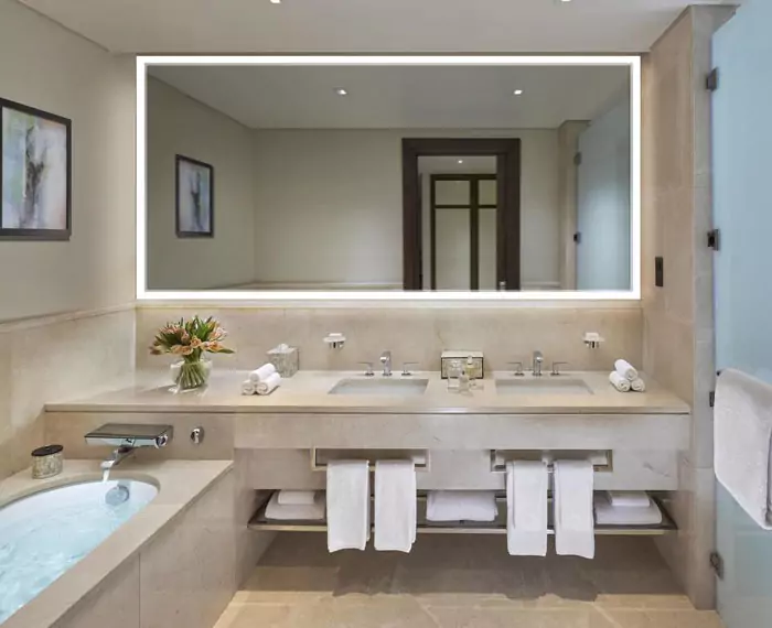 Fancy bathroom with an energy efficient mirror, a bathtub, and two sinks with towels below in Qatar.