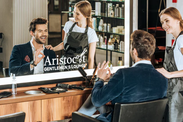 A man enjoying his hair with a stylist reflected in the barbershop logo in led mirror from Riyadh.