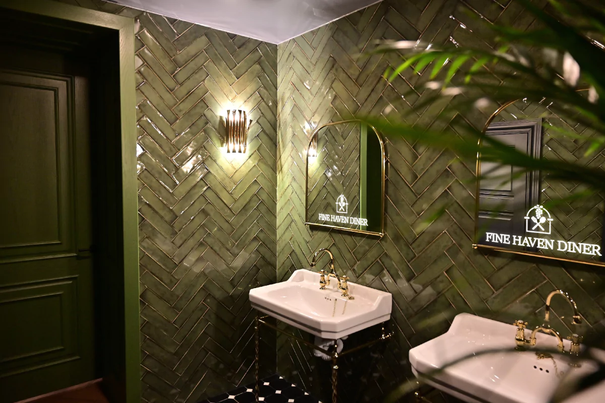 A green color bathroom with an arch shaped led light mirror with logo from Saudi Arabia.